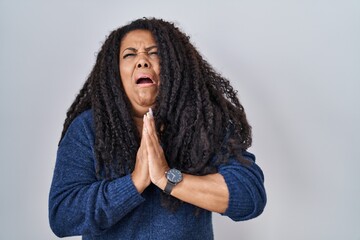 Fototapeta na wymiar Plus size hispanic woman standing over white background begging and praying with hands together with hope expression on face very emotional and worried. begging.