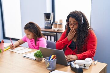 Mother and young daughter at the office working and doing homework covering mouth with hand,...