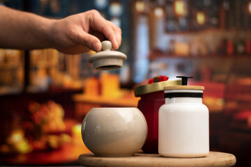 Hand open a Mug of sugar and salt containers style vintage over a table in night restaurant with selective focus and bokeh background