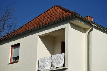 Weiße Hausfassade von Einfamilienhaus mit Federbettdecken zum Auslüften über Balkongeländer bei Sonne am Morgen im Frühling