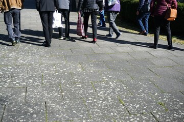 Gruppe von Menschen läuft über Platz mit grauen Steinplatten bei Sonne am Mittag im Frühling