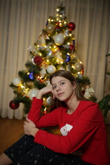 beautiful girl at home in pajamas sitting near the Christmas tree. red Christmas pajamas. the girl lit a sparkler near the Christmas tree. the magic of Christmas new year at home