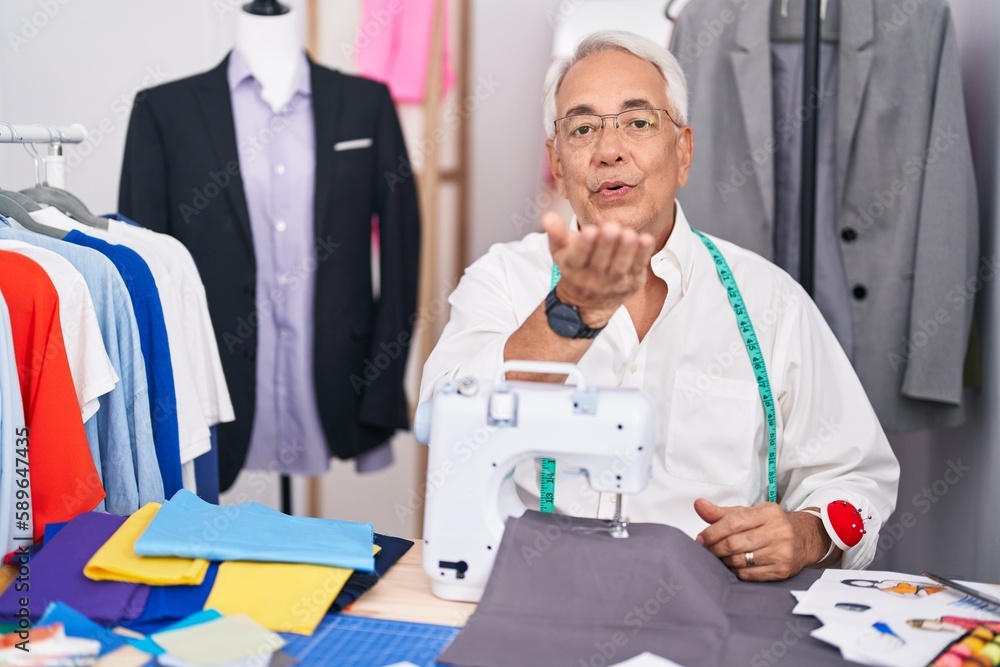 Poster middle age man with grey hair dressmaker using sewing machine looking at the camera blowing a kiss w