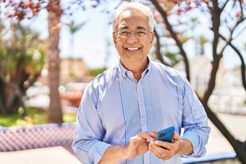 Fototapeta premium Senior man smiling confident using smartphone at park