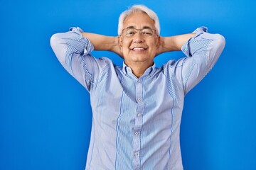 Naklejka premium Hispanic senior man wearing glasses relaxing and stretching, arms and hands behind head and neck smiling happy