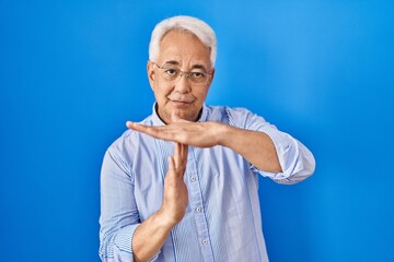 Hispanic senior man wearing glasses doing time out gesture with hands, frustrated and serious face