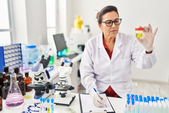 Middle age hispanic woman wearing scientist uniform analysing urine test at laboratory