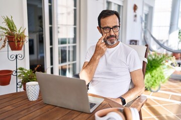 Middle age man using computer laptop at home pointing to the eye watching you gesture, suspicious expression