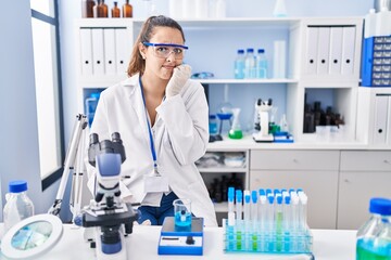 Fototapeta premium Young hispanic woman working at scientist laboratory looking stressed and nervous with hands on mouth biting nails. anxiety problem.