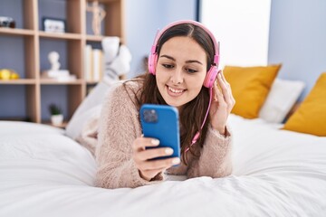 Young beautiful hispanic woman listening to music lying on bed at bedroom