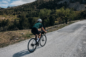 Fototapeta premium Woman cyclist riding a gravel bike with a view of the spanish mountains.Fit athlete wearing sportswear and helmet. Sports motivation image.