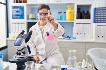 Fototapeta premium Hispanic girl with down syndrome working at scientist laboratory pointing with finger up and angry expression, showing no gesture