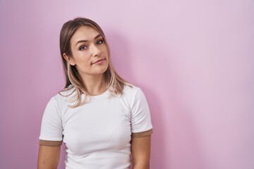 Blonde caucasian woman standing over pink background relaxed with serious expression on face. simple and natural looking at the camera.