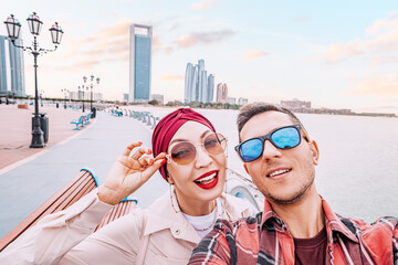 Adorable multicultural couple taking selfie photo on Abu Dhabi embankment with scenic view of...