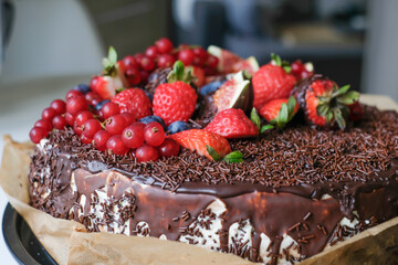 Delicious cake decorated with dark chocolate and fresh figs and blackberries, strawberries, currants. Appetizing chocolate cake with chocolate chips. Advertising for chocolate lovers. Bakery poster