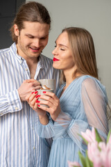 Beautiful young happy couple in light blue clothes enjoying coffee and each other's presence. Pink tulips in the corner in the foreground. Copyspace