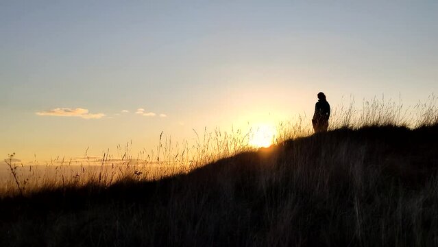 Sunset with the silhouette of a woman on a hillside during sunset