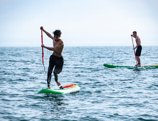 a sporty guy swims on a sup board with a paddle on the sea during the day against a beautiful sky