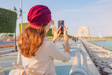 Embodying the spirit of modernity and progress in the UAE's capital city, a girl snaps a photo against the dazzling skyline of Abu Dhabi