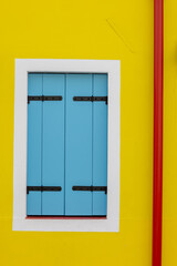 Colourful window shutters in Burano Venice, Italy. Yellow Background and white shutter frame. Typical colourful Italian door and window housing