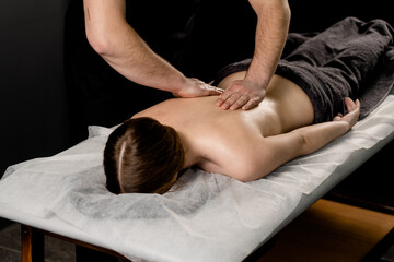 Attractive girl is relaxing on classic massage procedure in spa. Manual therapy. Masseur is doing back massage.