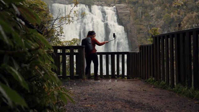 Woman taking selfie at waterfall with selfie stick. Social media and trevel concept