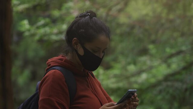Woman with face mask taking a selfie with her smartphone in the middle of the forest