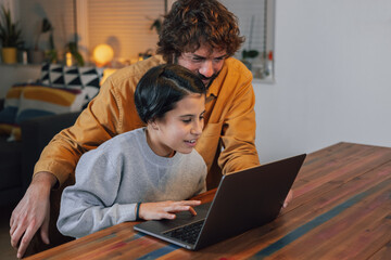 Hispanic teenage girl shows a game to young bearded man on tablet at home