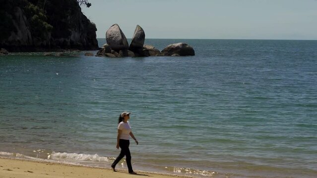 Woman walking by the beach with amazing Split Apple Rock in Abel Tasman National Park. New Zealand