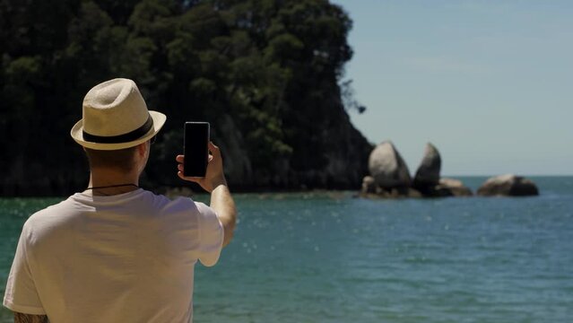 Man filming with smartphone at Split Apple rock formation, located in Abel Tasman National Park, New Zealand