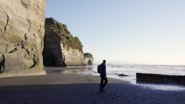 Caucasian man walking by Three Sisters and Elephant rock, New Plymouth coast. New Zealand