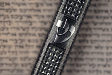 Mezuzah case laying on blurred parchment with Jewish prayer Shema Yisrael in hebrew, mezuzah commandment. Symbol of judaism. Closeup. Selective focus.