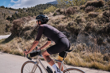 Male cyclist is conquering the challenging uphill terrain on his gravel bike.Sportsman training hard on bicycle in the mountains..Man cyclist  wearing cycling kit and helmet.Beautiful motivation image