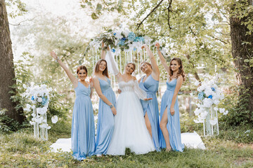 The bridesmaids in blue dresses raise their hands, rejoice, the bride is holding a beautiful...
