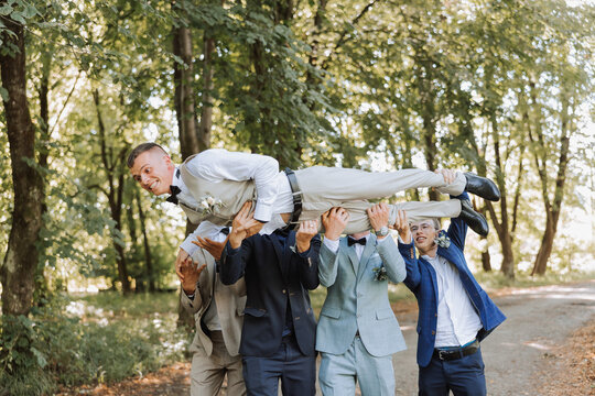 A group of friends lifts the happy groom to the top, the company of the groom's friends celebrate together in the park