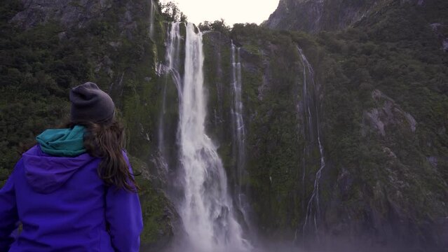 Young woman backwards looking at huge falls in Milford Sound. New Zealand travel destination