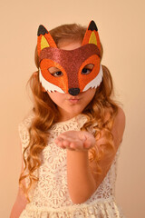 A child in a masquerade carnival mask of a fox, hand-made from glitter foamiran. Little cute cheerful comical girl in the role of a fox. The child is preparing for the carnival, holidays.