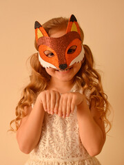 A child in a masquerade carnival mask of a fox, hand-made from glitter foamiran. Little cute cheerful comical girl in the role of a fox. The child is preparing for the carnival, holidays.