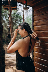 A girl takes a shower with fresh water on the beach or the street after sunburn, surfing and the sea Beautiful body, summer mood. Brunette in black swimwear enjoying natural water 