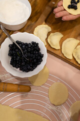 sculpt dumplings with blueberries. Cooking homemade blueberry dumplings. Ready dumplings, a piece of dough stuffed with berries and a colander with blueberries