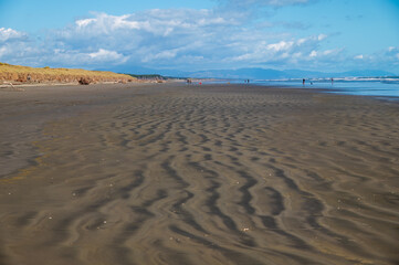 deserted sandy Foxton Beach looking south  with sand ripples. In the distance a few people and the Tararua mountains