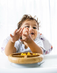 Baby eating fruit and clapping. Mention the health of children in food and strengthening of the...