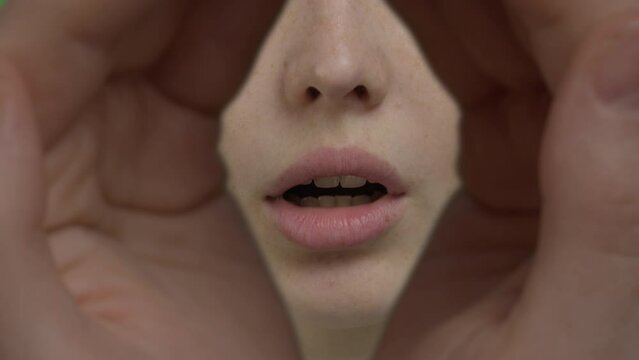 female palms are connected to form a hole through which you can look or peep, Extreme close-up of the face of a white red-haired girl whispering with her lips