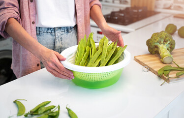 A girl in a pink shirt and a white t-shirt stands in the kitchen at home and is going to cook a vegetarian diet food. Concept of a healthy nutrition and veggie lifestyle. Green vegetables on the table