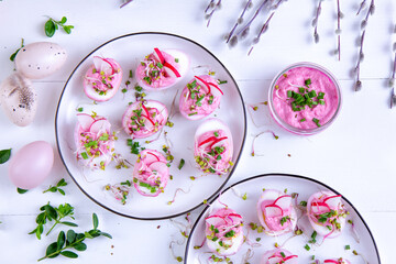 Pink eggs dyed with beetroot juice stuffed with horseradish filling with radish, sprouts and chives. Easter egg dish.