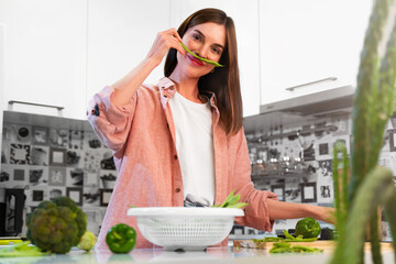 Happy Young beautiful woman making mustache from green bean on face at home kitchen and smiles. The concept of a healthy nutrition and vegan lifestyle. Healthy food for detox. Copy space