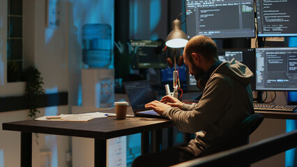 Database programmer typing server code on multiple screens using coding language on laptop late at...