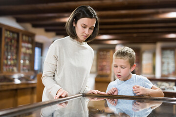 Attentive young woman with school age boy exploring artworks in glass case in museum