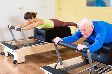 Fototapeta na wymiar Older man doing exercises of remedial gymnastic on Pilates reformer in rehab clinic. Physical medicine concept ..