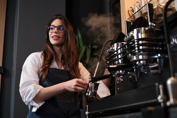 Barista standing next to a coffee machine in a coffee shop and heating up milk.